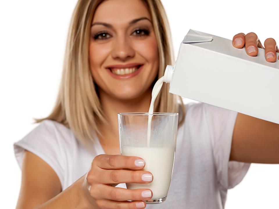 image of a smiling woman pouring a glass of milk from a carton